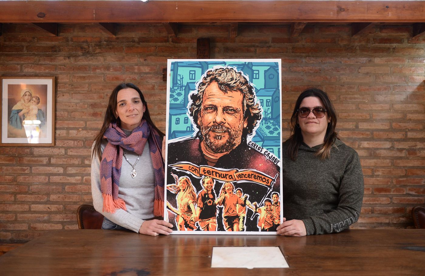 Agustina y Lidia hoy, sosteniendo una imagen de Carlos Cajade en la parroquia del Hogar.