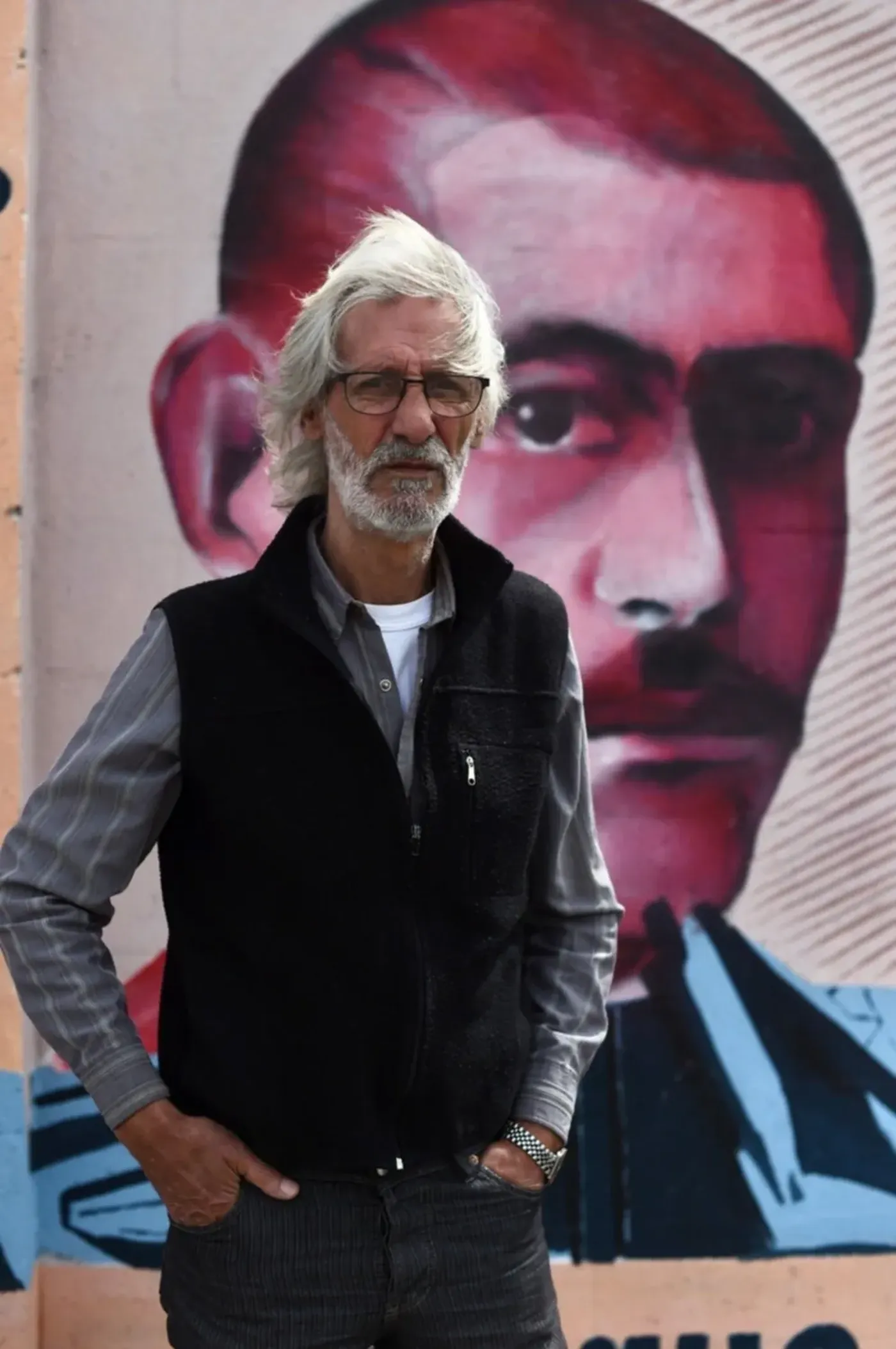 El Flaco Rodolfo Ortiz y detrás un mural con el rostro de su padre, el Cholo, caído en el bombardeo al Barrio Campamento